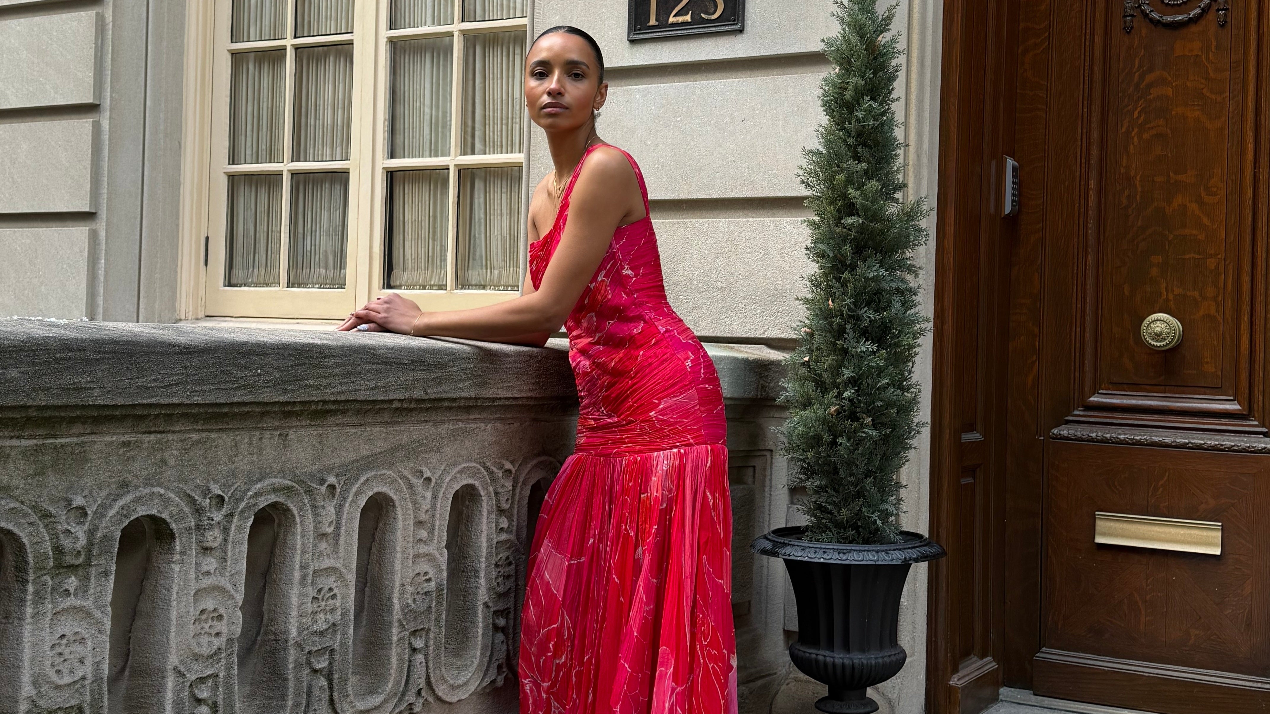 Woman in a red dress leaning against a building entrance in NYC